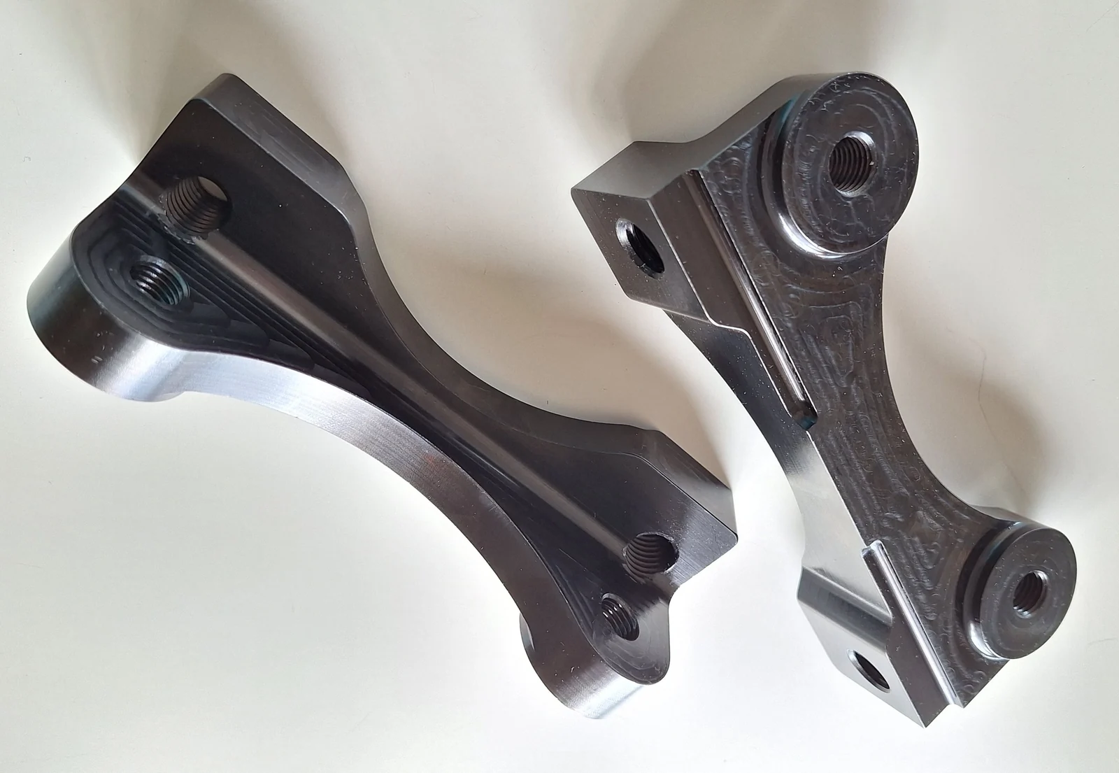 Two machined caliper mounting brackets showing threaded mounting holes